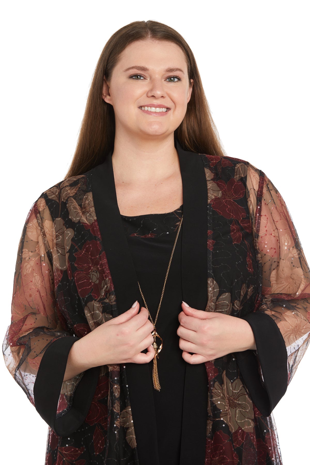 A woman smiles, wearing the R&M Richards 3312W Plus-Size Jacket Party Dress with a sheer floral-patterned jacket over a black top, holding the lapels; white background.